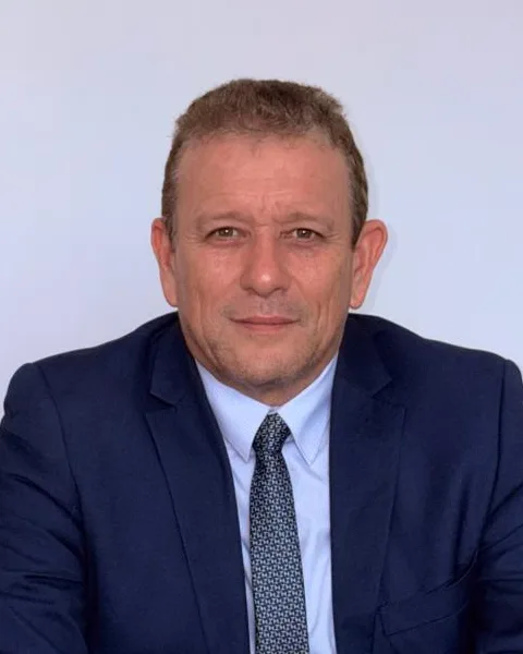 Silmar Silva, de terno, sentado à mesa do escritório da corretora, olhando para a câmera.